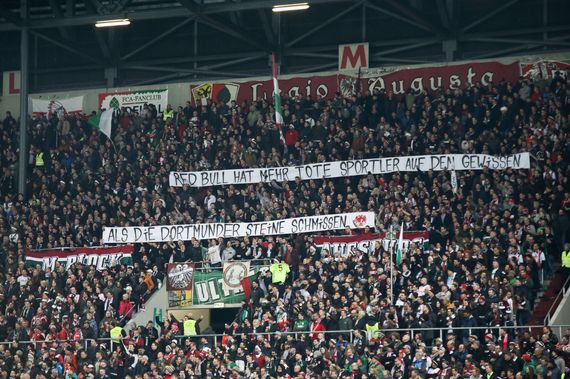Spruchband im M-Block mit Anspielung auf verunglückte Extremsportler, die von Red Bull gesponsort wurden.<br />Bild: Sport-in-Augsburg.de”><figcaption>Spruchband im M-Block mit Anspielung auf verunglückte Extremsportler, die von Red Bull gesponsort wurden.<br />Bild: Sport-in-Augsburg.de</figcaption></figure>
<figure><img decoding=