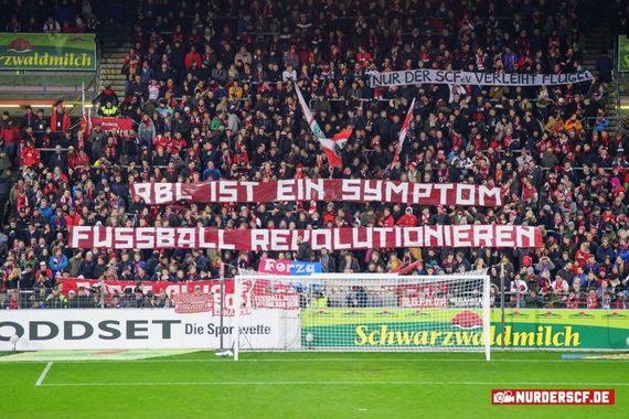 Spruchband auf der Freiburger Nordtribüne.<br />Bild: nur-der-scf.de”><figcaption>Spruchband auf der Freiburger Nordtribüne.<br />Bild: nur-der-scf.de</figcaption></figure>
<figure><img decoding=