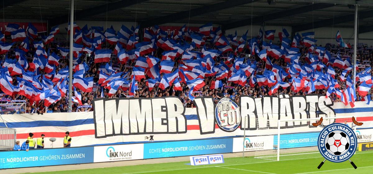 Das Block 501-Fahnenmeer heute in Kiel.<br />Bild: Calcio-Culinaria.de”><figcaption>Das Block 501-Fahnenmeer heute in Kiel.<br />Bild: Calcio-Culinaria.de</figcaption></figure>
<figure><img decoding=