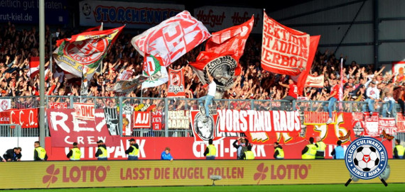 Die Fans des 1. FC Köln beim Auswärtsspiel in Kiel.<br />Bild: Calcio-Culinaria.de”><figcaption>Die Fans des 1. FC Köln beim Auswärtsspiel in Kiel.<br />Bild: Calcio-Culinaria.de</figcaption></figure>
<figure><img decoding=