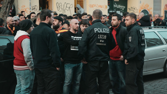 Der stellvertretende Europakoordinator von ultrAslan, Ogulcan Sariboga, im Gespräch mit Polizei beim Basketballspiel Alba Berlin gegen Galatasaray Istanbul in Berlin.<br />Bild: www.kinostar.com”><figcaption>Der stellvertretende Europakoordinator von ultrAslan, Ogulcan Sariboga, im Gespräch mit Polizei beim Basketballspiel Alba Berlin gegen Galatasaray Istanbul in Berlin.<br />Bild: www.kinostar.com</figcaption></figure>
<figure><img decoding=