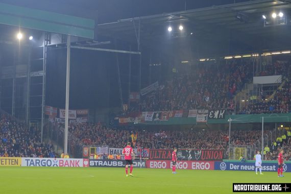 Als Union-Fans Zaunfahnen im Oberrang platzierten, eskalierte die Lage.<br />Bild: Nordtribuene.org”><figcaption>Als Union-Fans Zaunfahnen im Oberrang platzierten, eskalierte die Lage.<br />Bild: Nordtribuene.org</figcaption></figure>
<figure><img decoding=